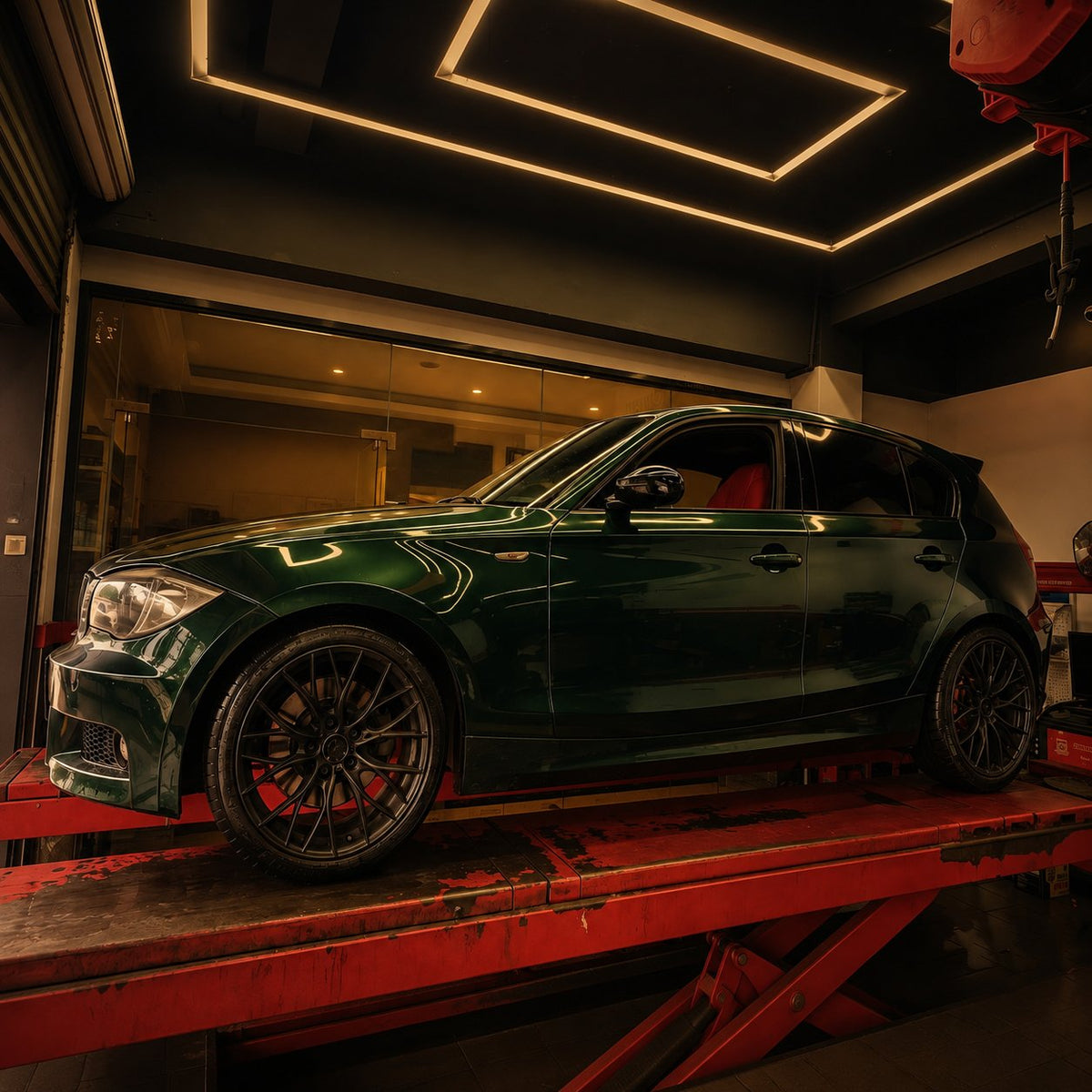 BMW 1 Series on car lift in moody dark workshop with warm amber light for VREL About Us community section